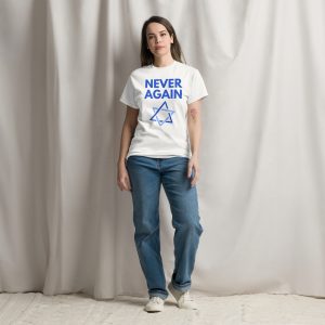A woman standing against a neutral fabric backdrop, wearing a white T-shirt with the text &ldquo;NEVER AGAIN&rdquo; and a blue Star of David design, paired with jeans and sneakers.